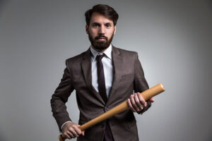 A bearded man in a business suit brandishes a baseball bat