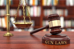 The scales of justice, along with a judge's gavel resting on a gun laws plate.