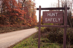 A "hunt Safely" Sign On The Side Of A Dirt Road In The Fall Wood