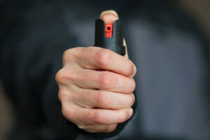 A pepper spray can is held properly, with the thumb depressing the spray and the grip in an upright position