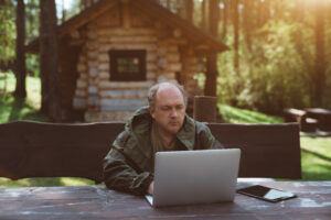Hunter on laptop with cabin in woods in background