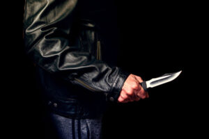 Man in black leather jacket holds a knife.