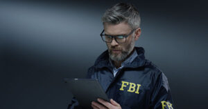 An FBI agent in traditional windbreaker makes notations on a clipboard.
