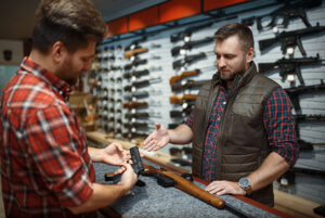A gun store customer examines a pistol while the clerk shows him features.