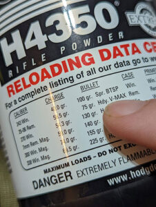 A person's finger runs along reloading data printed on the back of a container of powder