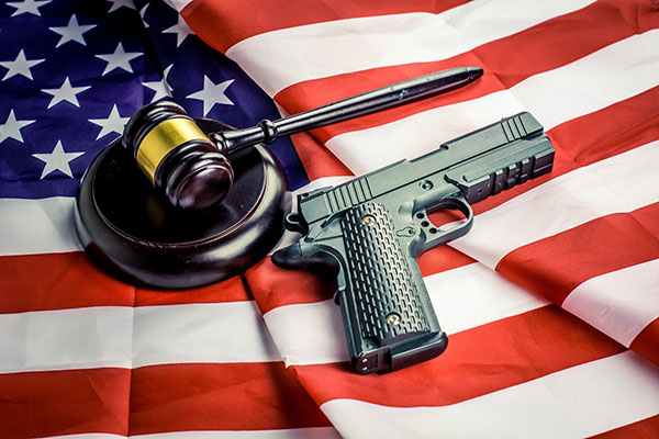 A pistol rests on an American flag next to a gavel.