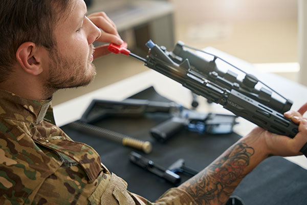 A man wearing cammo cleans the barrel of a rifle 